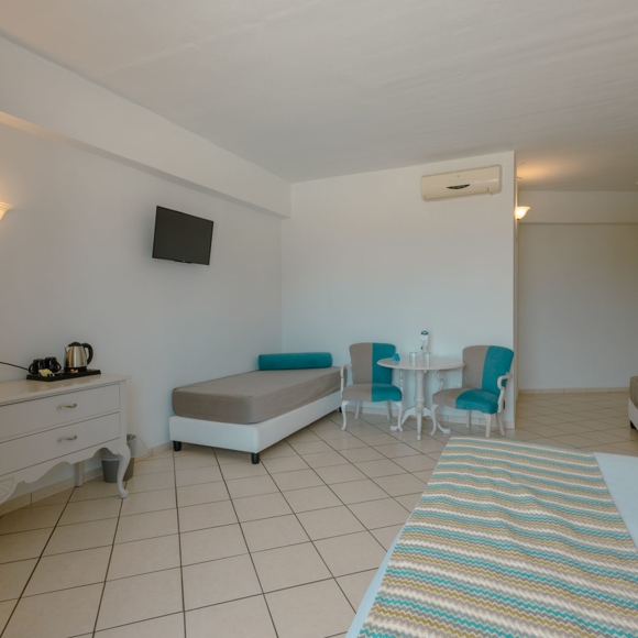 Quadruple room interior with two single beds, vanity desk, armchairs and a wall-mounted TV