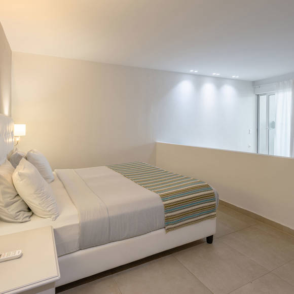 Double bed with wall-mounted lamps with partial view of the sitting area
