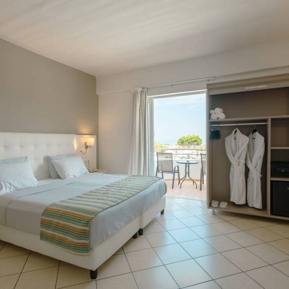 Quadruple room with a double bed, open wardrobe, a safe, vanity desk, and a balcony overlooking the sea