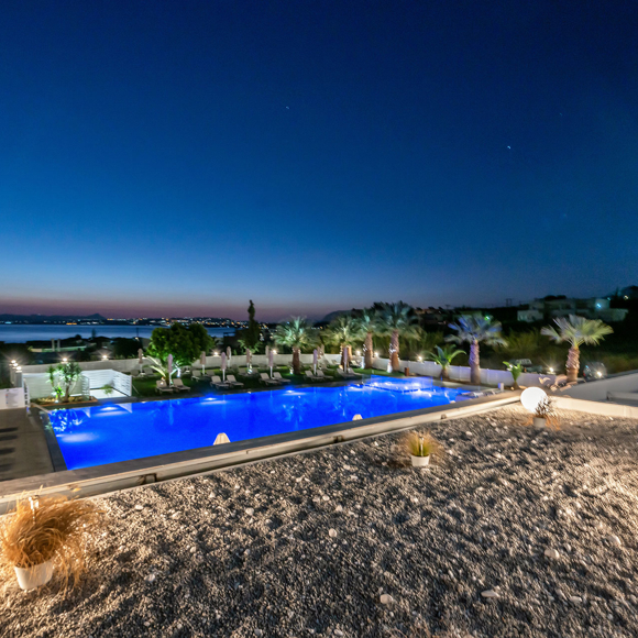 Hotel pool and garden illuminated at night with sea view in the background