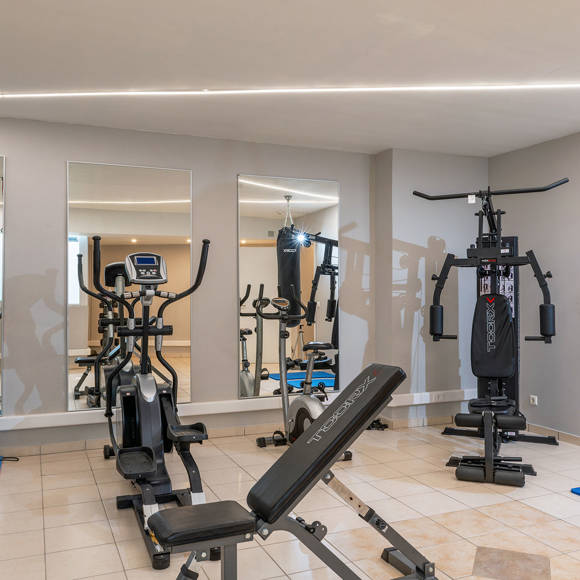 Modern indoor gym with treadmills, elliptical machines, weight bench, and multi-exercise station