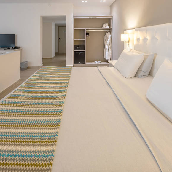 Close up side view of a double bed with white headboard and open wardrobe 