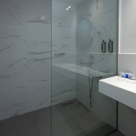 Modern bathroom with marble-style walls, mirror, and minimalistic white sink with amenities