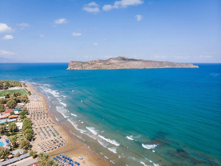 Dore hotel beach with sunbeds, umbrellas, a calm blue sea and view of Theodorou Island