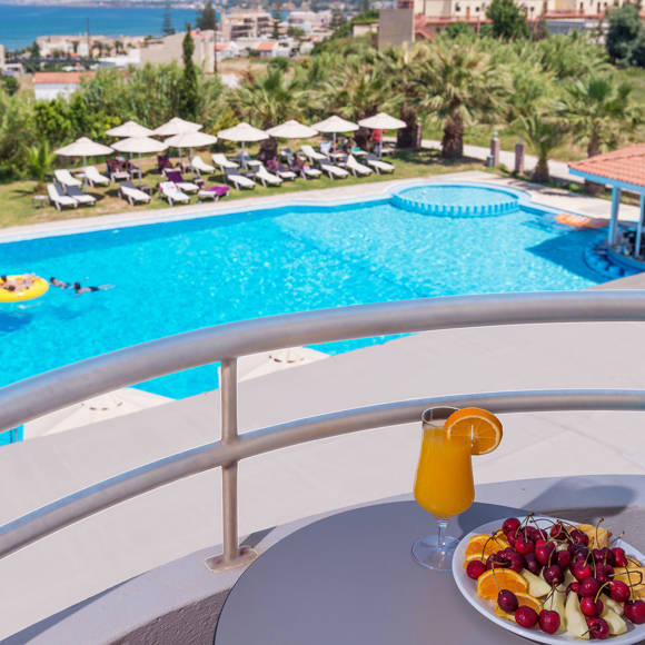 Balcony view of the hotel pool with sunbeds, and the sea in the background