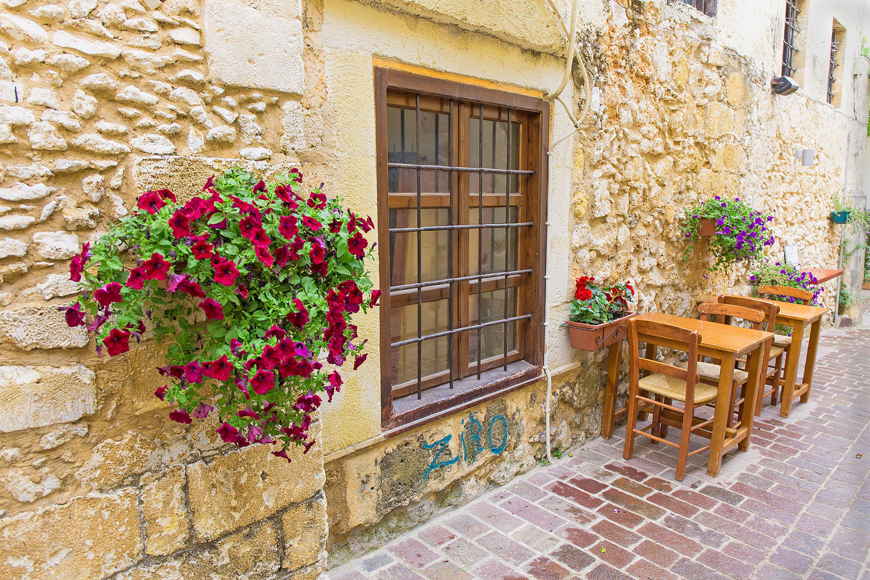 Traditional alley in Chania with stone walls, flowers and wooden tables
